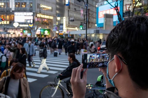 A tourist films the crowd at the zebra crossing of Shibuya Crossing with his smartphone,