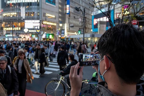 A tourist films the crowd at the zebra crossing of Shibuya Crossing with his smartphone,