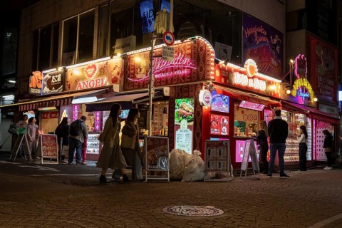 Tourists in front of a shop with illuminated advertisement for kebab and Japanese crepes in