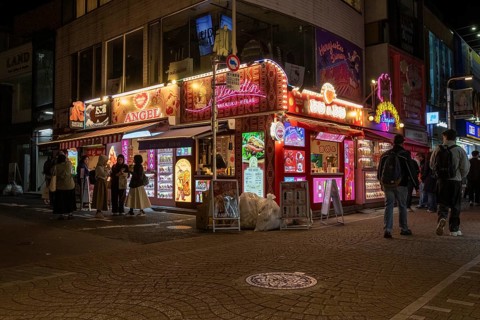 Tourists in front of a shop with illuminated advertisement for kebab and Japanese crepes in