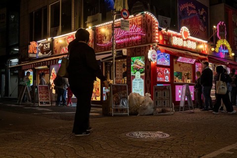 Tourists in front of a shop with illuminated advertisement for kebab and Japanese crepes in