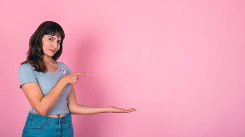 Young woman pointing and presenting with a pink ribbon for breast cancer awareness and copy space