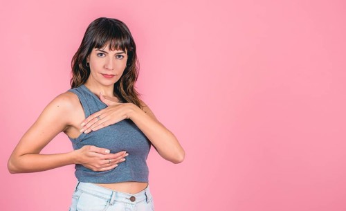Young woman performing self-breast exam against pink background with copy space
