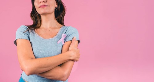 Young woman embracing herself with a pink breast cancer awareness ribbon and copy space