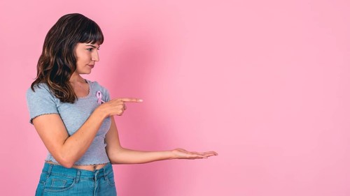 Young woman pointing and presenting with a pink ribbon for breast cancer awareness and copy space