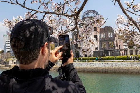 Tourist taking a photo of cherry blossoms with a smartphone, sakura, behind it atomic bomb dome,
