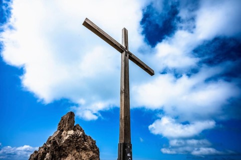 A wooden cross on a rock under a blue sky with white clouds. Kleinwalsertal Vorarlberg Austria