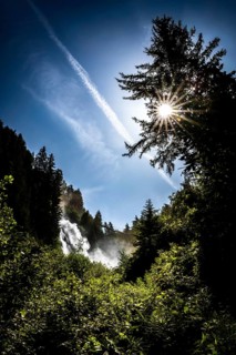 A waterfall in the forest under a bright sun and blue sky. Stuibenfall Austria Ötztal