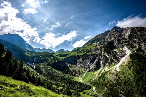 Sunny mountain scene with green slopes and dramatic clouds over the mountains. Kleinwalsertal