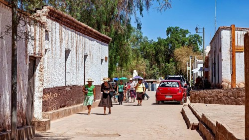 Pedestrians in summer clothes walk along a street with white buildings and a red car, The town of