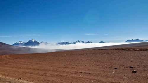 Dry desert plain with distant mountains and wafts of mist under a clear sky, The landscape at San
