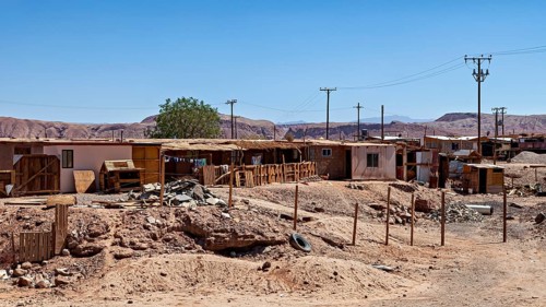 An arid landscape with simple buildings and electricity pylons under a clear sky, The town of San