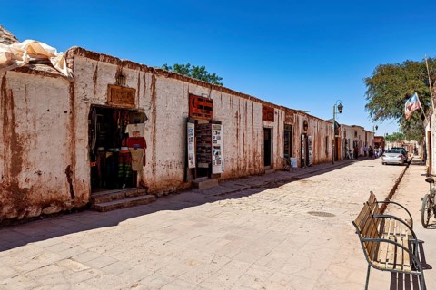 A quiet stretch of street with shops in old buildings along a cobbled path under a blue sky, The