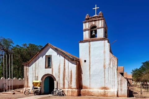 Historic church with bicycle in front of a clear blue sky, cross on the bell tower, The church of