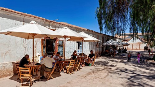 People sit in a café under parasols on the sunny street next to an old building, The town of San