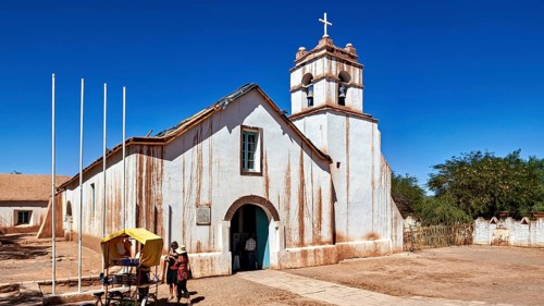 Church under a clear blue sky with people in the foreground and a cross on the tower, The church of