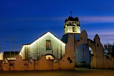 Church at dusk with illuminated tower and cross in front of a deep blue sky, The church of San