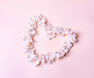 Heart made of mother-of-pearl white shells, on beige background, copy space