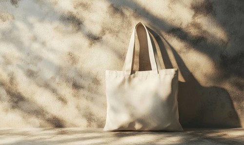A white canvas bag is sitting on a table in front of a wall. The bag is empty and the wall is made
