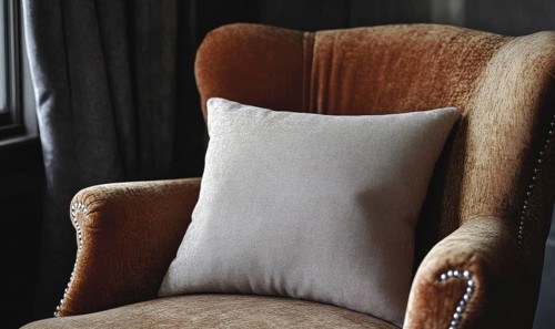 A brown chair with a white pillow on it. The pillow is fluffy and has a pattern on it. The chair is