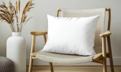 A white pillow sits on a wooden chair in front of a vase. The chair is a simple design with a zebra