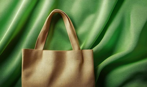 A brown purse is on a green background. The purse is made of a woven material and has a gold trim.