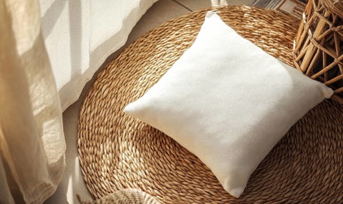A white pillow sits on a woven rug in front of a window. The pillow is unoccupied and the rug is