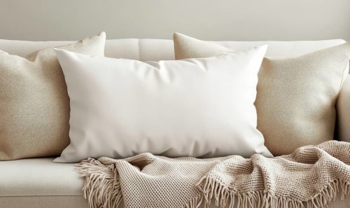 Cozy sofa setup with beige pillows, a large white pillow, and a fringed blanket in a neutral