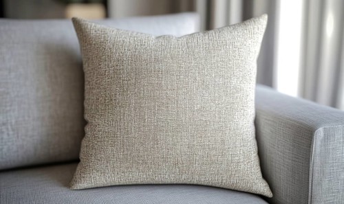 A pillow with a pattern on it sits on a couch. The pillow is white and has a texture that looks