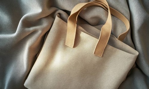 A tan purse with a brown strap sits on a grey cloth. The purse is open and the strap is visible. AI