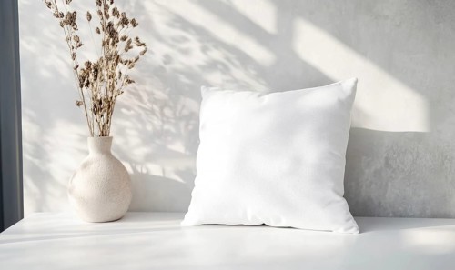A white pillow sits on a table next to a vase of flowers. The pillow is unmade and the flowers are