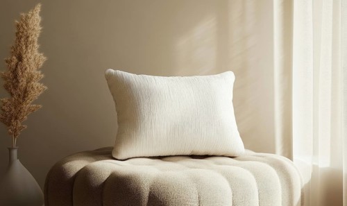A white pillow sits on a white cushion. The pillow is placed on a round cushion, which is also