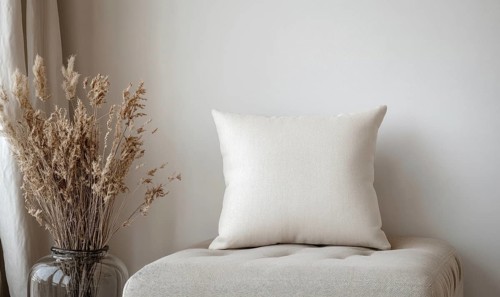 A white pillow sits on a bench next to a vase of dried flowers. The pillow is unmade and the