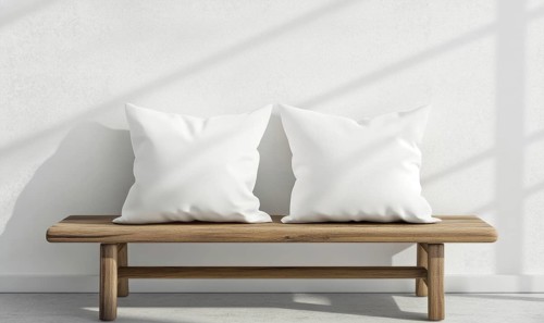A wooden bench with two white pillows on it. The bench is located in a room with a white wall and a