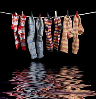 Clothesline with some multicolored sox fixed with clothes pins over reflective water surface in