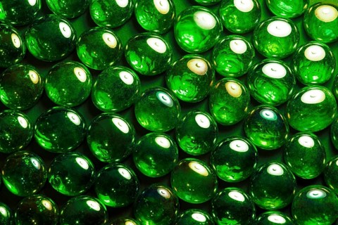 Full frame abstract background picture with iridescent green glass beads in dark back