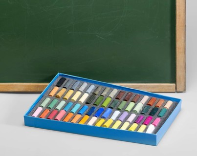 Edge of a old used blackboard and a box of crayons in front. Studio photography in light grey back