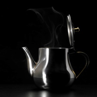 Studio photography of a steaming metal tea pot in dark back