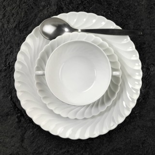 Studio photography of white porcelain plates and spoon on dark stone surface seen from above