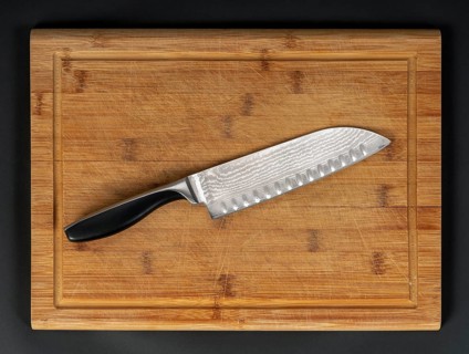 Pattern-welded knife on wooden bamboo cutting board in dark back