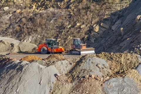 Roller compactor and bulldozer in stony hillside ambiance