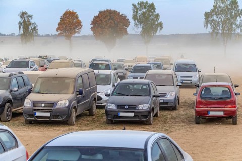 Dusty parking space scenery on a field including lots of dust covered cars at evening time in