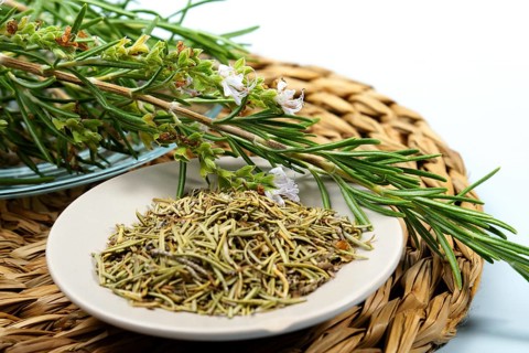 Fresh rosemary sprigs with flowers lie on a plate of dried rosemary, ready for culinary or