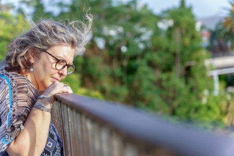 Grey-haired senior woman wearing glasses, leans on a railing, lost in contemplation amidst a serene