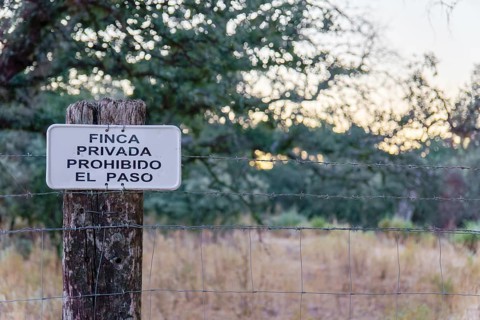 No trespassing sign in spanish (finca privada, prohibido el paso) attached to a barbed wire fence
