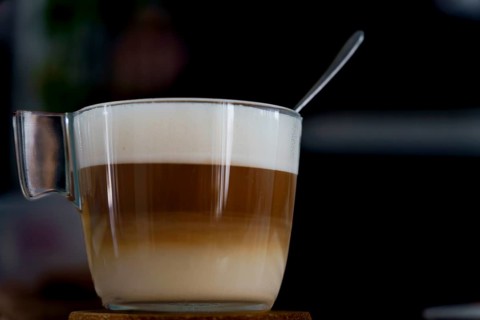 Latte macchiato in a glass cup with a spoon resting on the foam, showing the distinct layers of