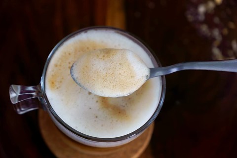 Creamy coffee foam being lifted by a spoon from a glass cup, creating a close-up view of the rich