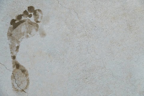 Muddy footprint marking a gray concrete surface with cracks, symbolizing evidence, trace, or
