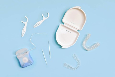 Top view of dental clear aligners, case, toothpicks and floss on blue background