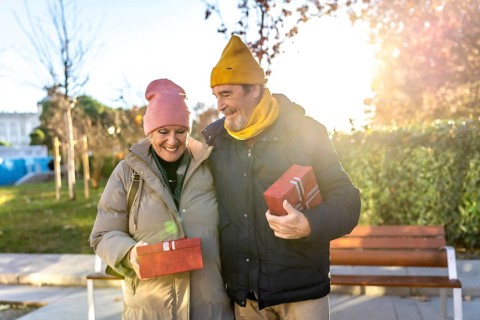 Smiling senior couple exchanging christmas gifts while walking in a city park during a sunny winter